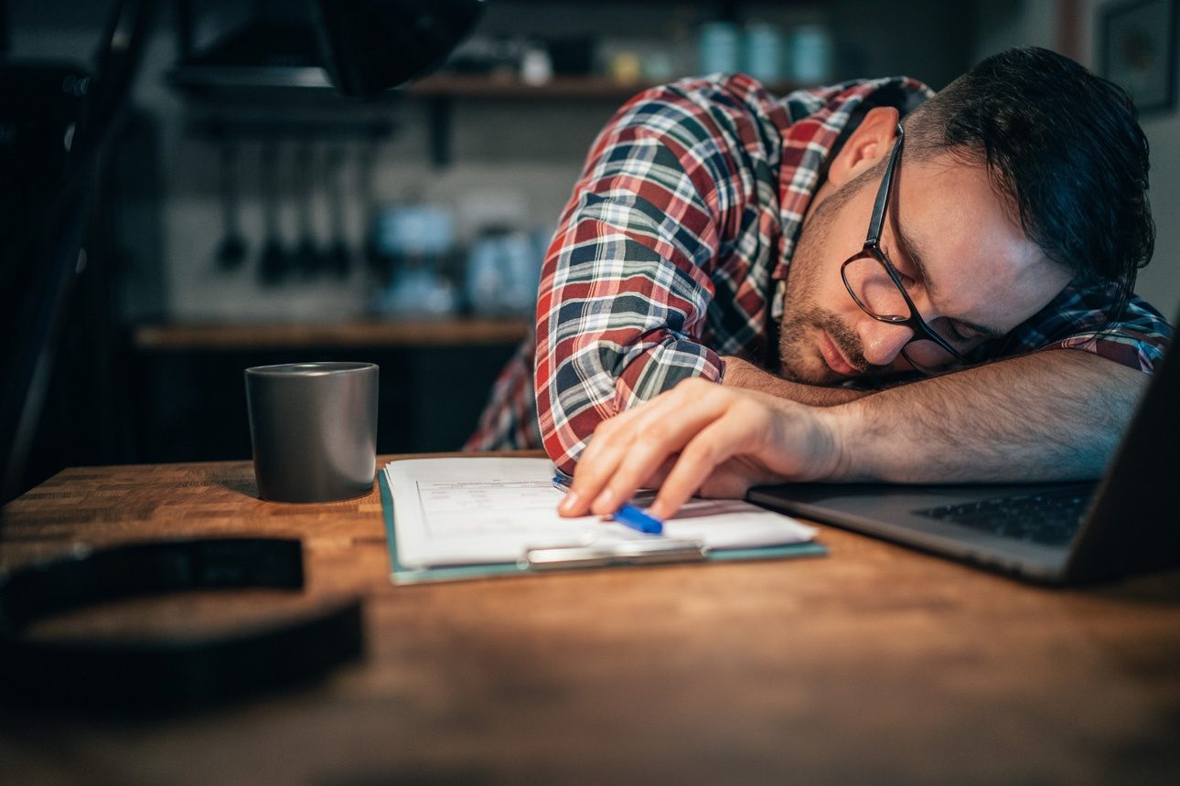 Un homme assoupi sur son bureau, devant son ordinateur