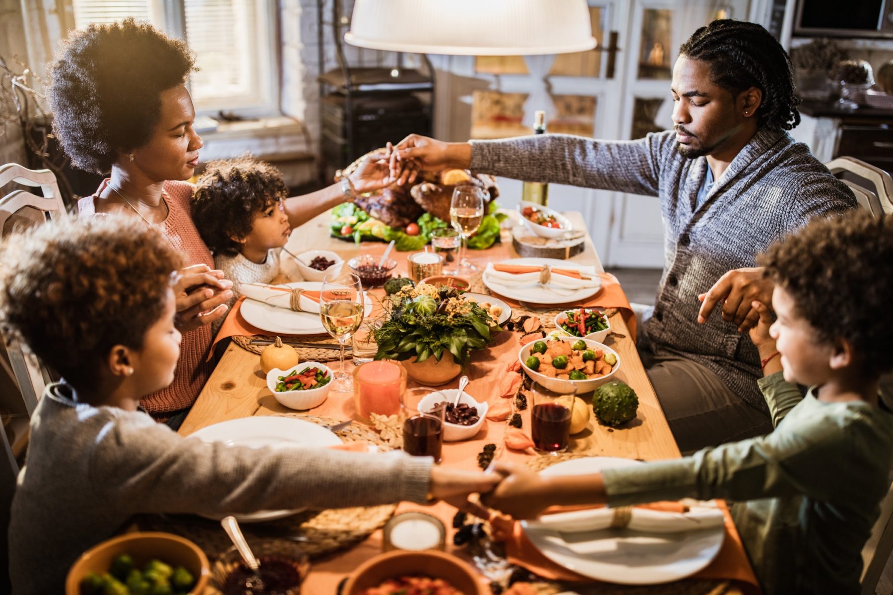 Famille afro-américaine se tenant la main et priant avant leur repas de Thanksgiving à la maison.