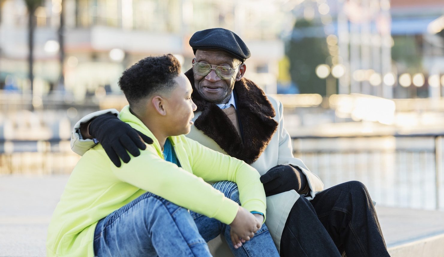 Un garçon afro-américain de 10 ans assis avec son arrière-grand-père de 79 ans, traînant sur un front de mer de la ville, en automne ou en hiver. Le vieillard a son bras autour de l'épaule de son arrière-petit-fils, lui donnant des conseils. Ils ont des expressions sérieuses sur leurs visages.