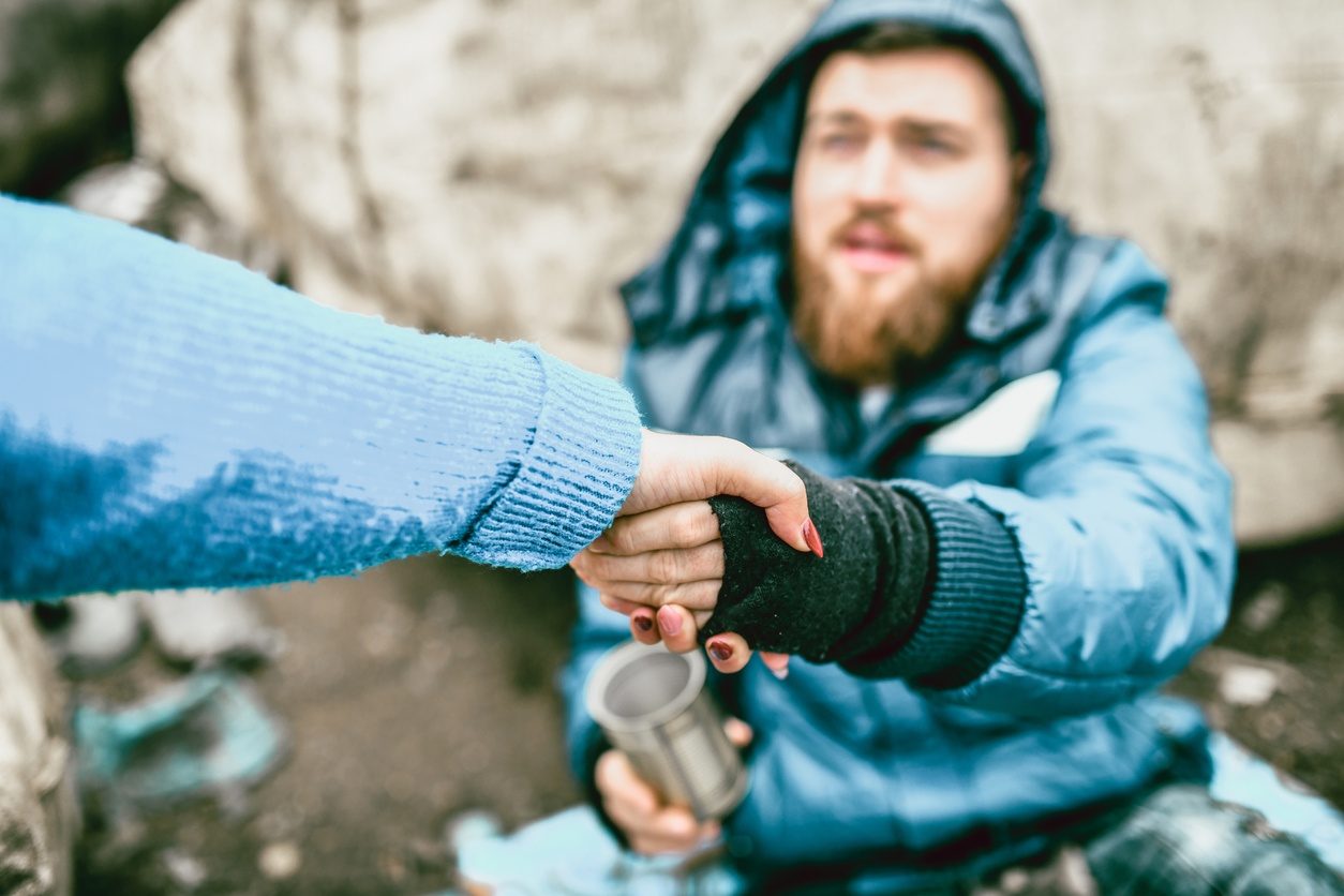 Une femme tend la main à un sans abri dans la rue