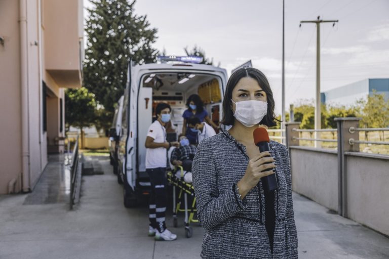 Une journaliste portant un masque rapporte les dernières nouvelles devant un hôpital pendant une pandémie