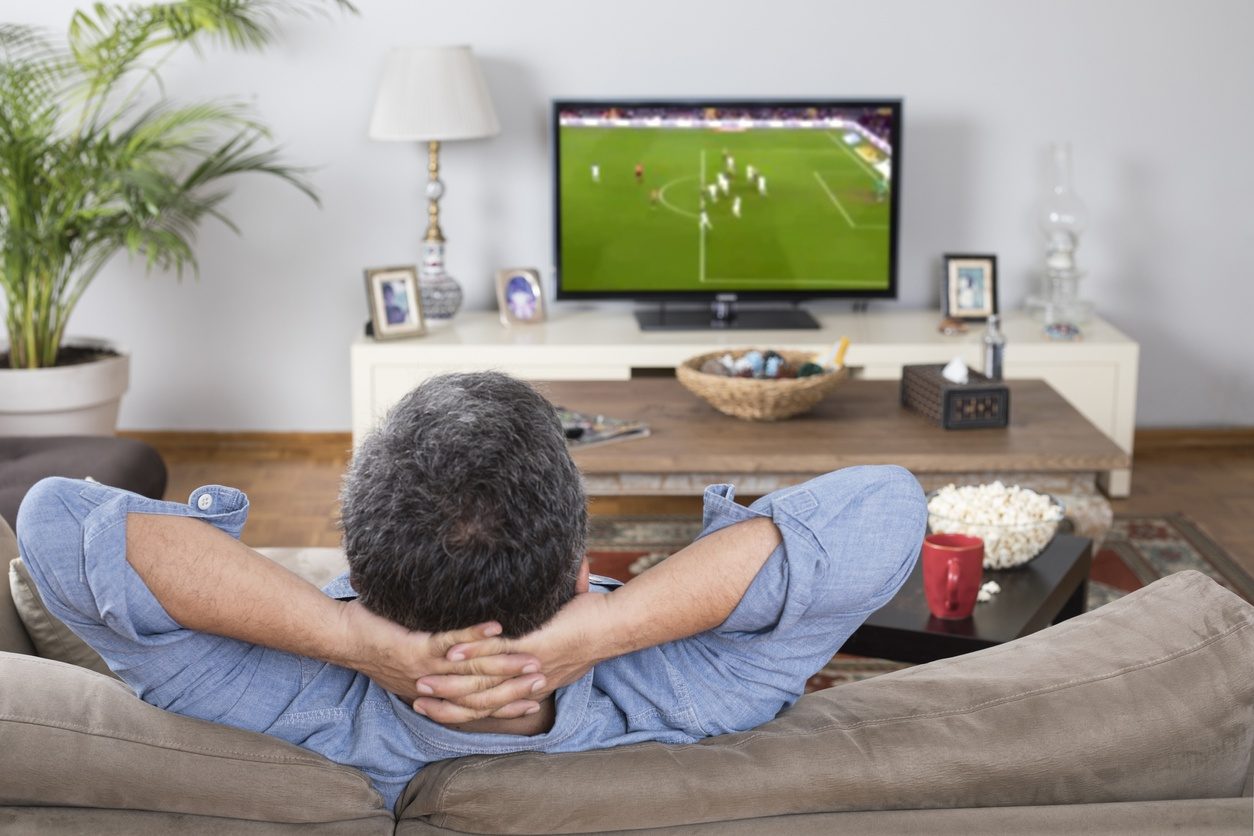 Un homme regardant un match de football à la télévision, bien installé dans son canapé.