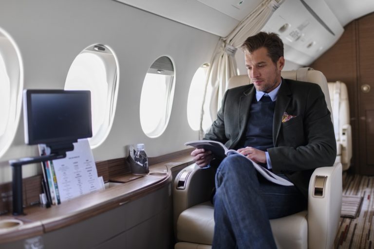 Un homme assis à l'intérieur d'un avion privé et lisant un magazine pendant le vol.