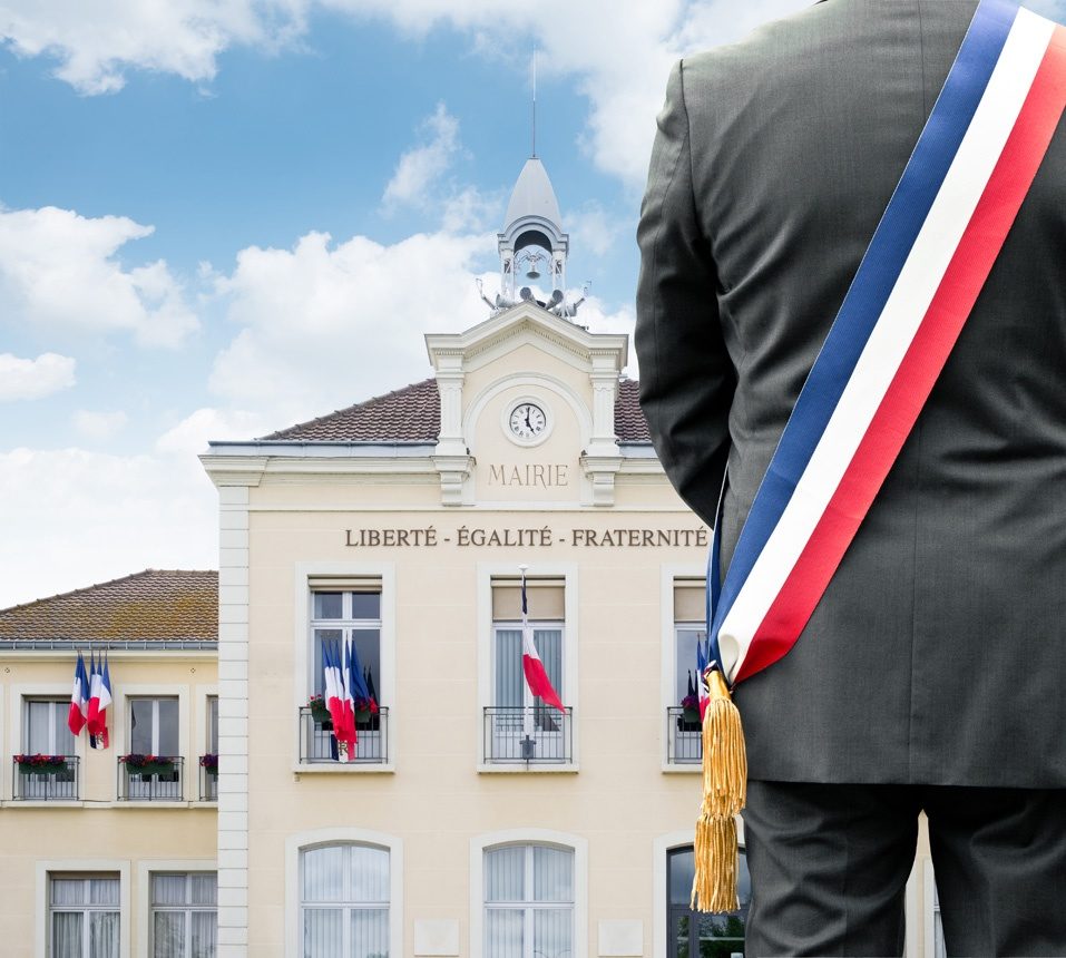 Un maire avec son écharpe tricolore devant sa mairie