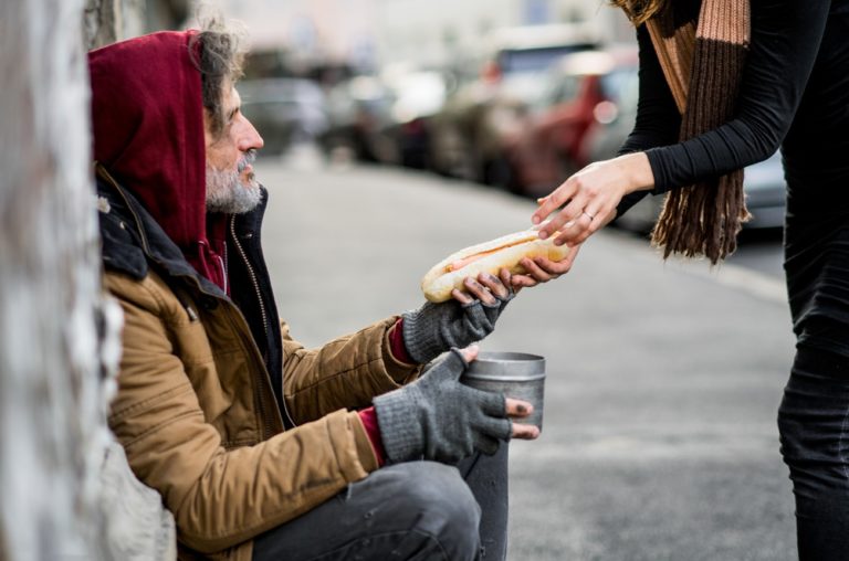 Une femme donnant de la nourriture à un mendiant sans-abri assis dans la rue.