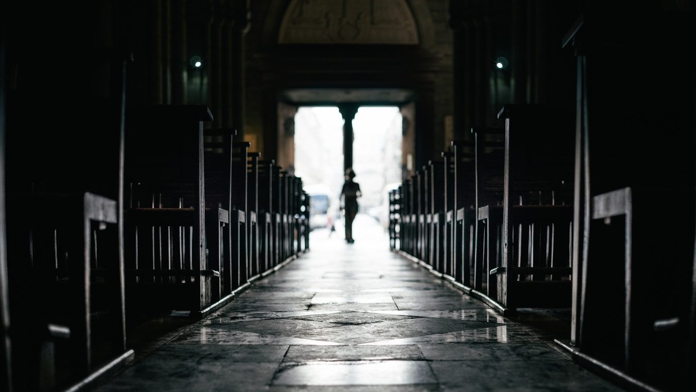 Des rangées de bancs à l'intérieur d'une église silencieuse avec des passants venant de la sortie