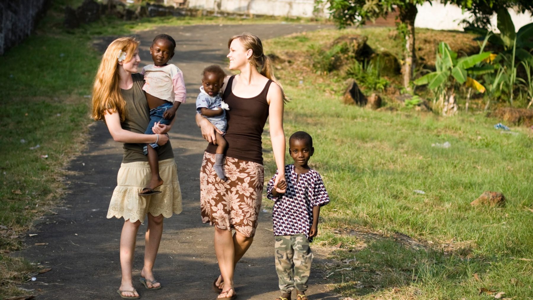 Deux femmes blanches qui tiennent par la main ou dans les bras des enfants en bas âges d'origine africaine.