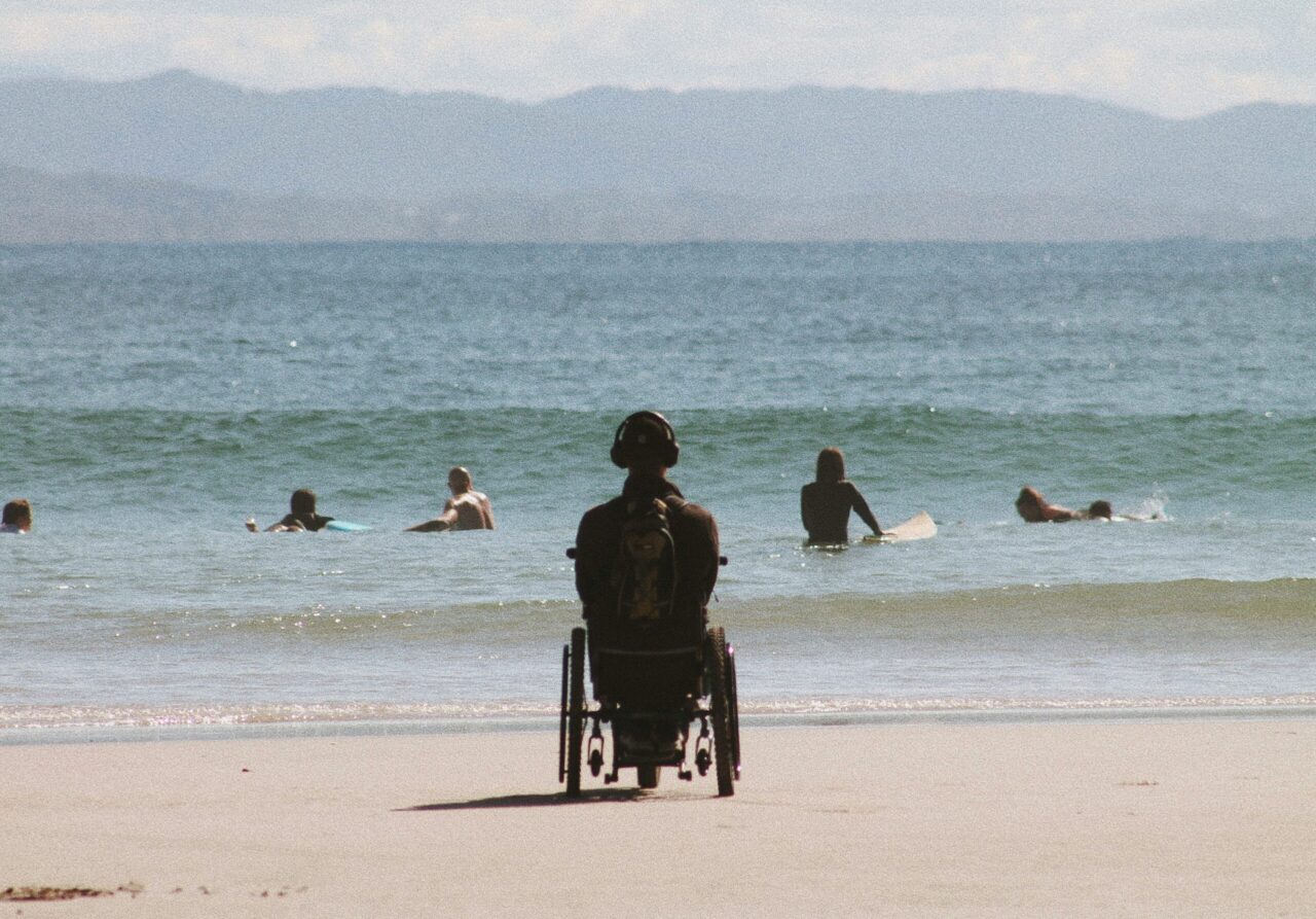 Une personne en fauteuil roulant sur une plage, regard tourné vers la mer