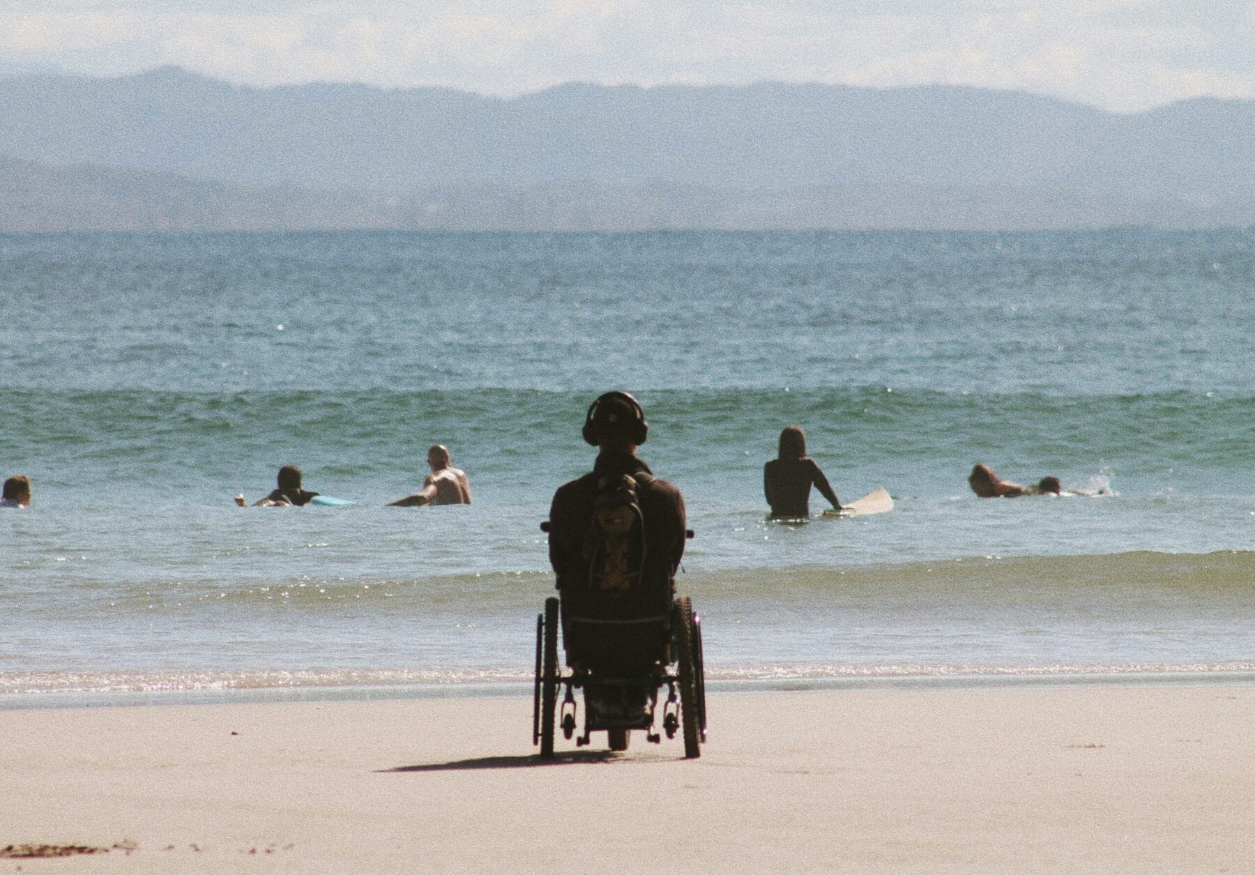 Une personne en fauteuil roulant sur une plage, regard tourné vers la mer
