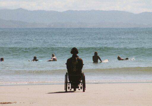 Une personne en fauteuil roulant sur une plage, regard tourné vers la mer