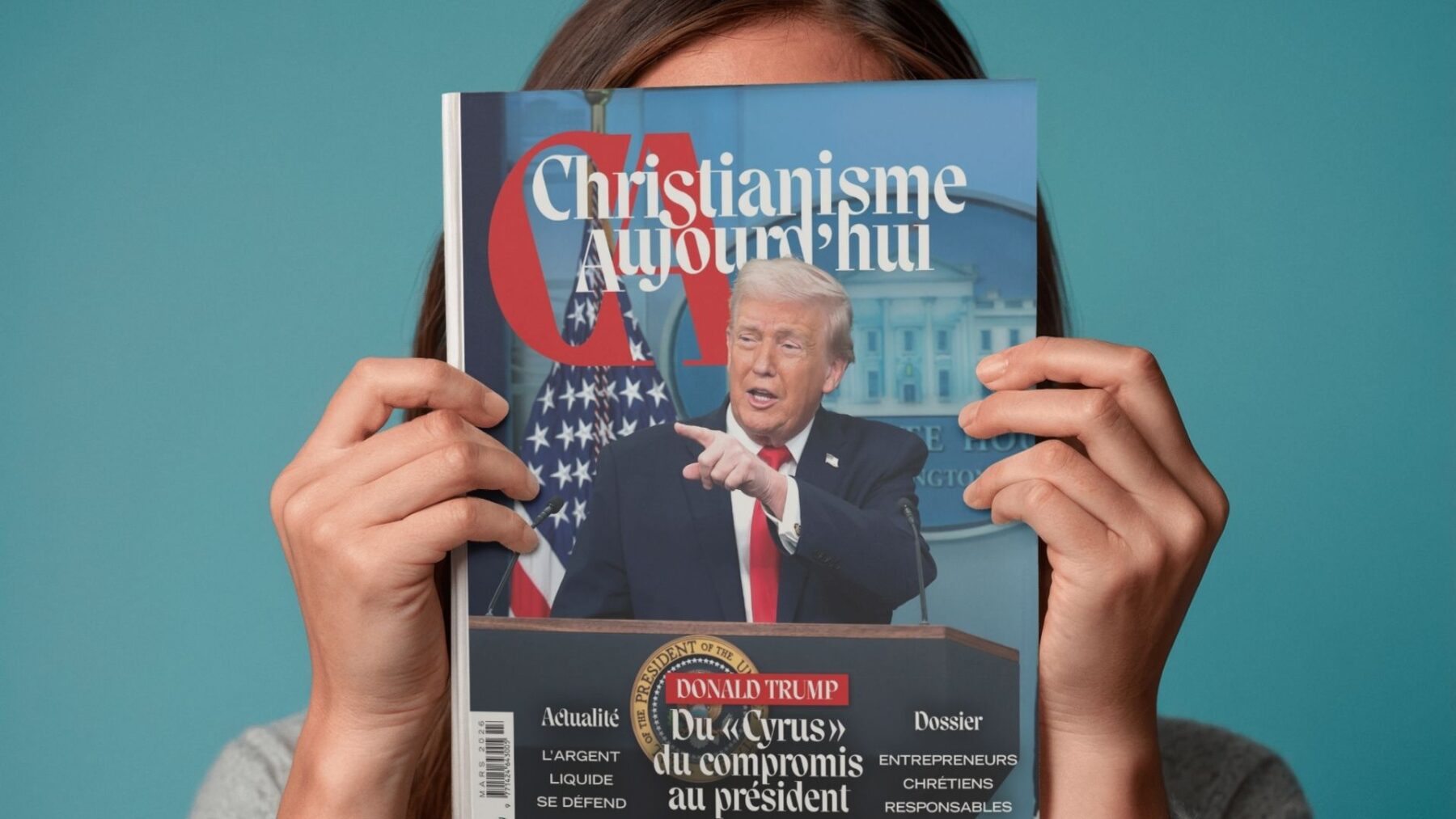 Femme tenant devant sa tête le magazine de mars, dont la une présente une photo de Donald Trump
