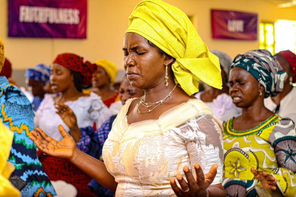 Une femme nigériane en prière, paumes ouvertes, au sein d'une assemblée