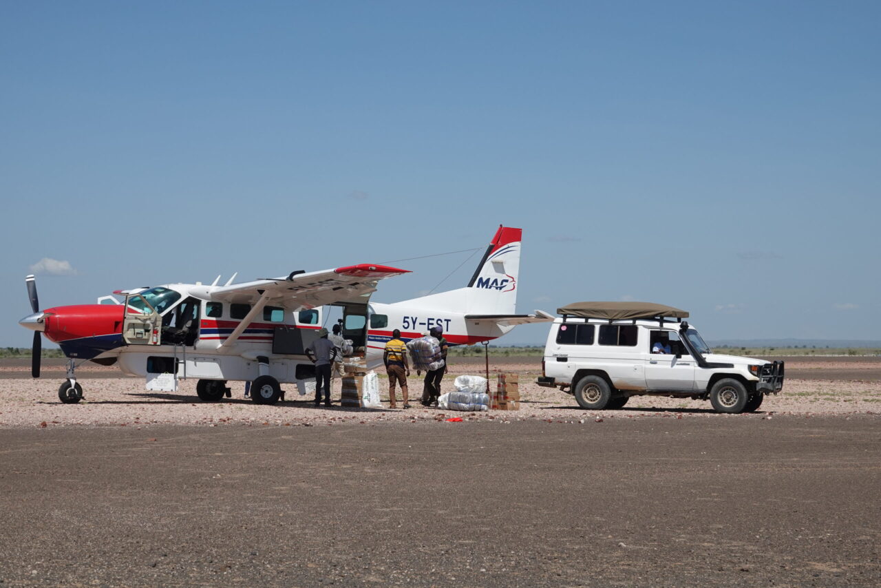 Avion de la MAF posé sur une piste en terre battue, avec véhicule tout-terrain