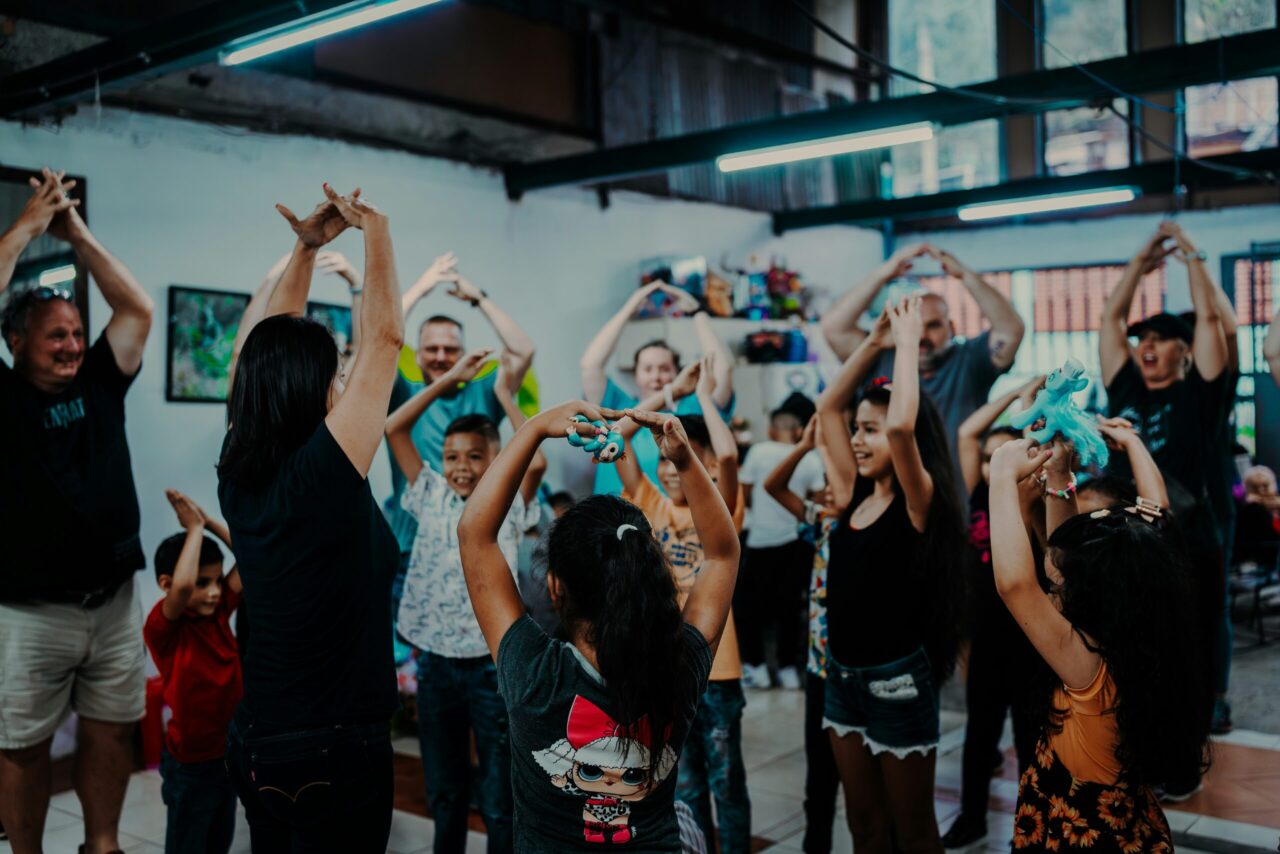 Groupe d'enfants et d'adultes levant les mains en forme de cœur lors d'une mission humanitaire.
