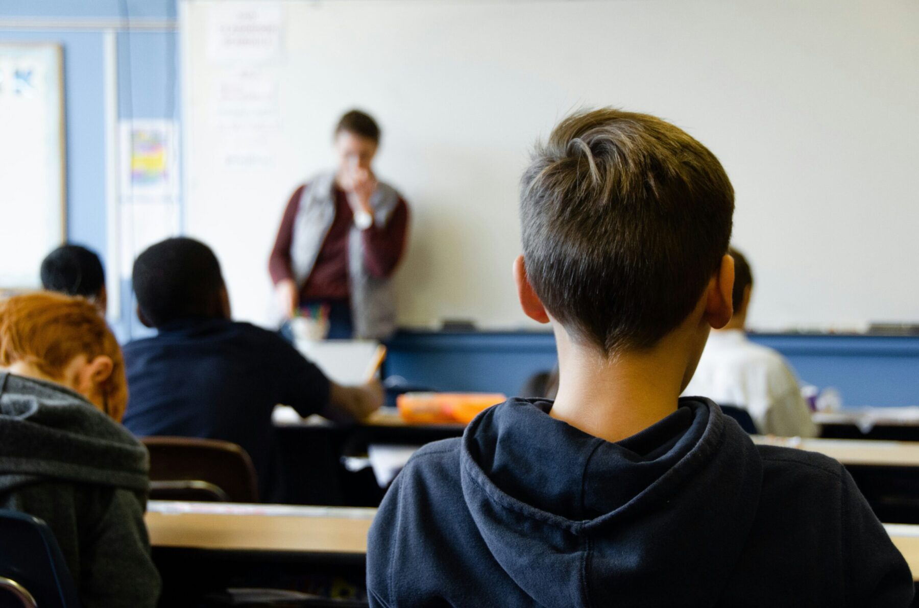 Enseignant s'adressant à des élèves en classe, enfant de dos au premier plan