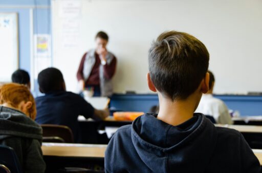 Enseignant s'adressant à des élèves en classe, enfant de dos au premier plan