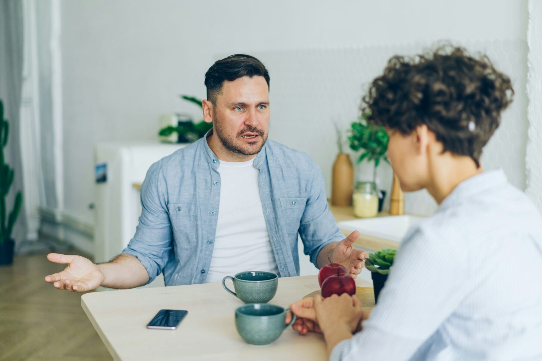 Un homme et un adolescent discutent face à face, assis à une table où sont posées deux tasses et un téléphone