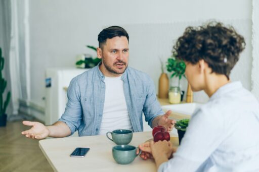Un homme et un adolescent discutent face à face, assis à une table où sont posées deux tasses et un téléphone