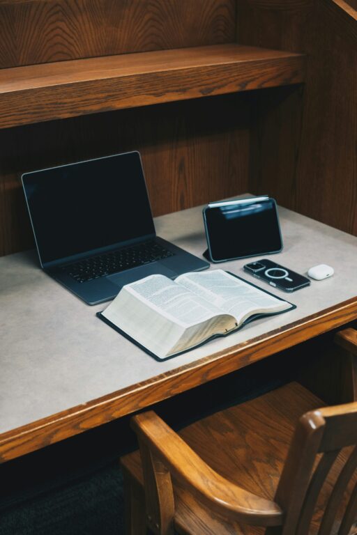 Une Bible, un ordinateur portable et un téléphone posés sur un bureau en bois