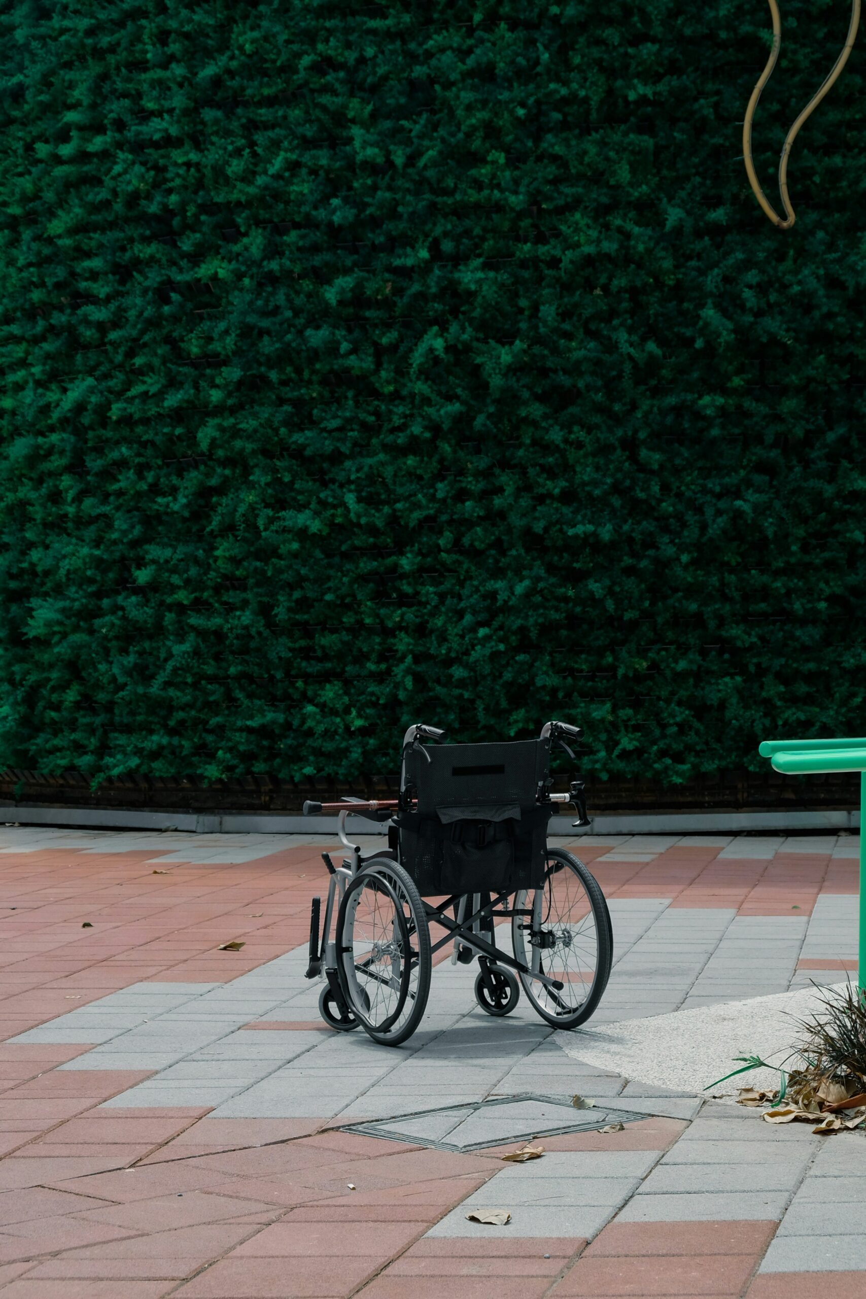 Fauteuil roulant vide stationné sur une terrasse, devant une haie verte taillée