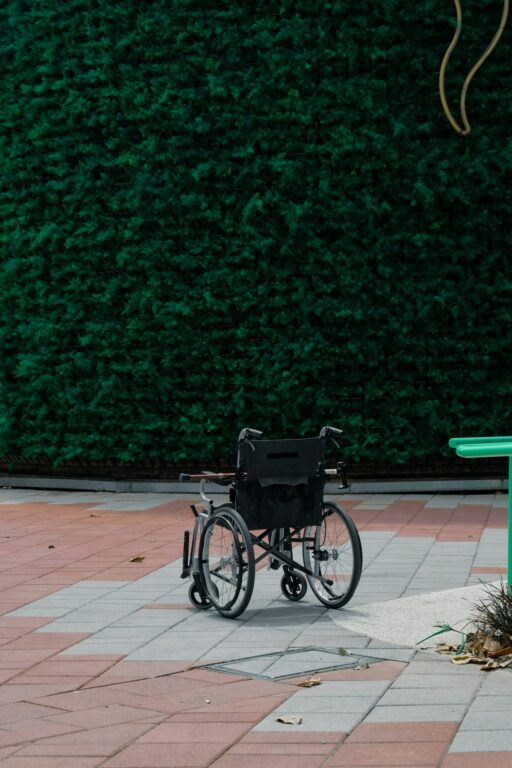 Fauteuil roulant vide stationné sur une terrasse, devant une haie verte taillée