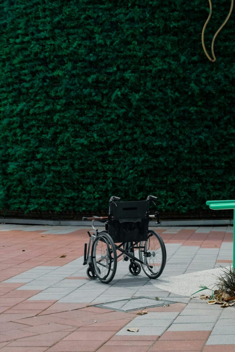 Fauteuil roulant vide stationné sur une terrasse, devant une haie verte taillée